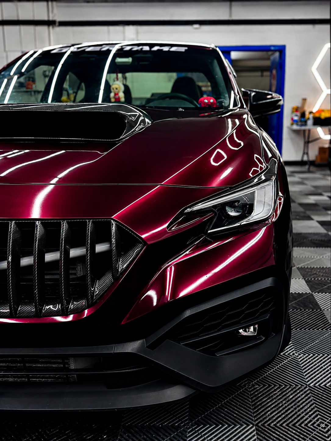 Burgundy performance sedan with a mirror-like ceramic-coated gloss inside the CustomsByAli shop in Elyria, OH