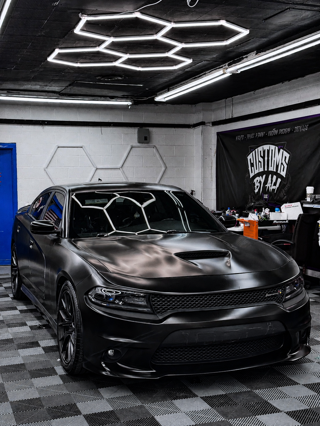 Dodge Charger in a satin black color change wrap under hexagon shop lighting at CustomsByAli