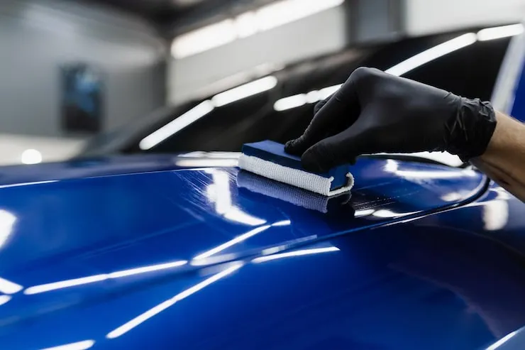 Installer laying down a ceramic coating on a blue hood at the CustomsByAli shop in Elyria, OH